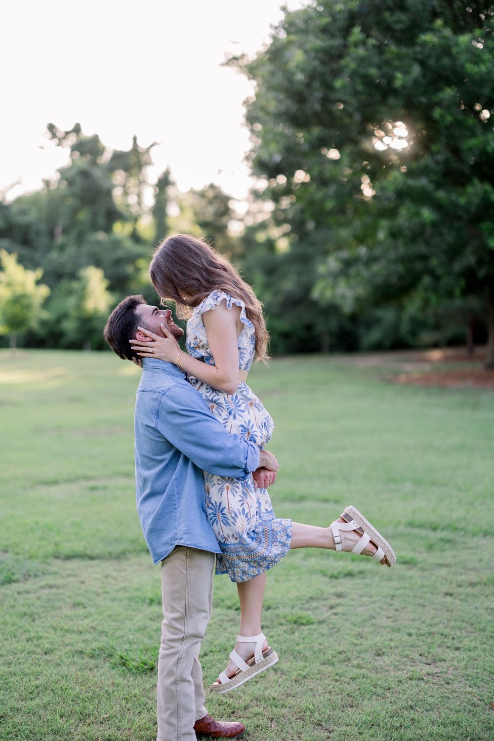 A couple shares romantic moments together on a grassy hill during a sunset photoshoot.