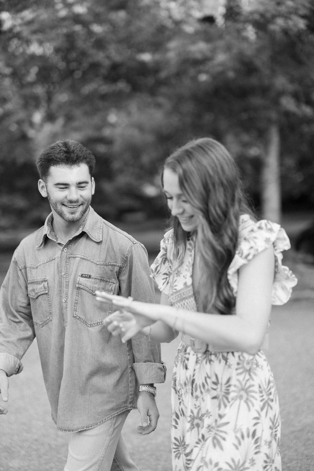 A playful couple in denim and floral dress share a joyful moment together in a black and white outdoor photo series.
