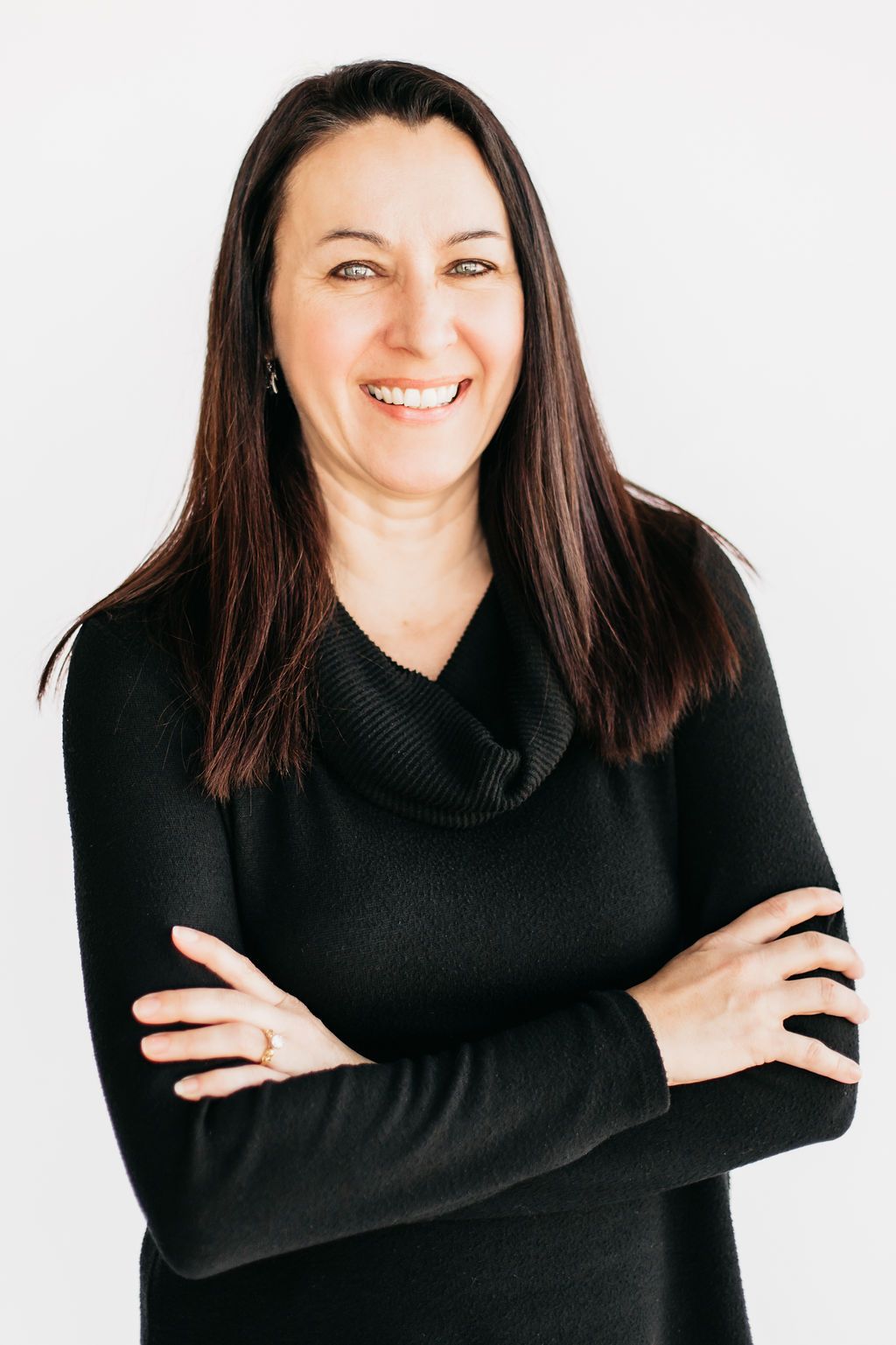 Smiling woman with dark hair, arms crossed, wearing a black cowl-neck sweater, posing against a white background.