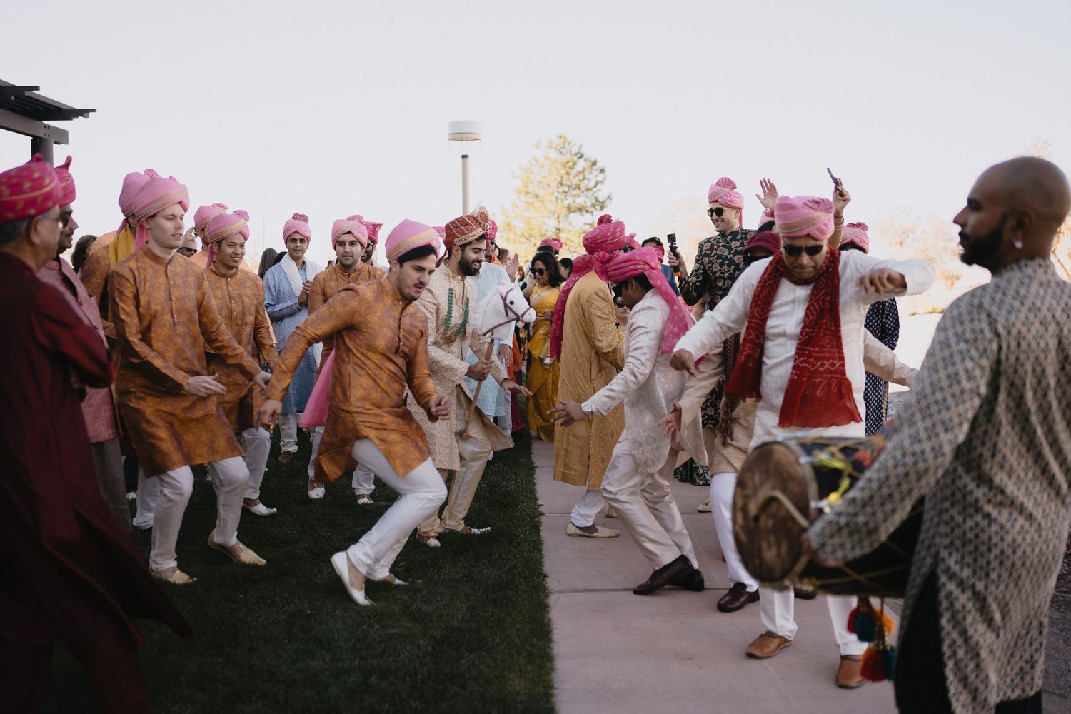 Groomsmen in orange kurtas and pink turbans dancing energetically during Indian wedding baraat.at Sandia Resort and Casino