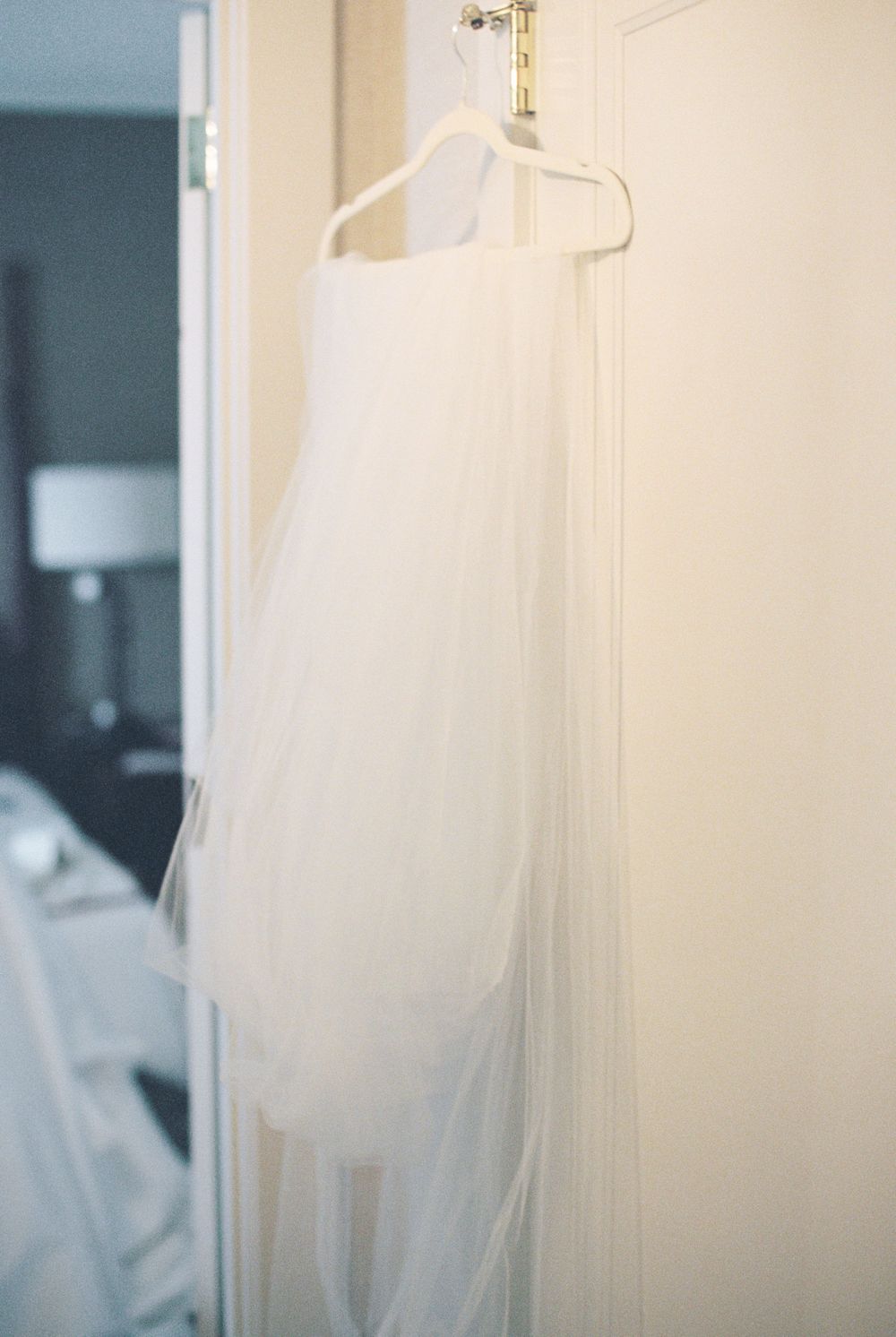 Elegant white tulle wedding dress details hanging against a light colored wall.