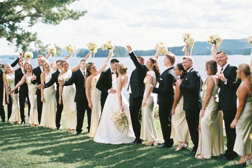 Wedding party members lined up outdoors striking fun poses against a scenic waterfront backdrop.