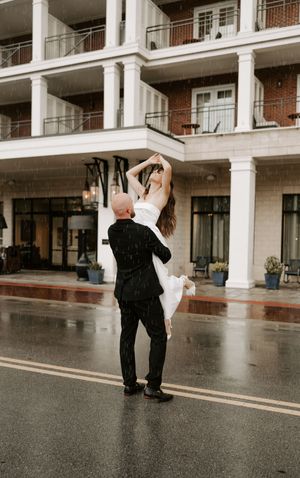 Dancing in the rain outside a colonial style building during wedding celebration.