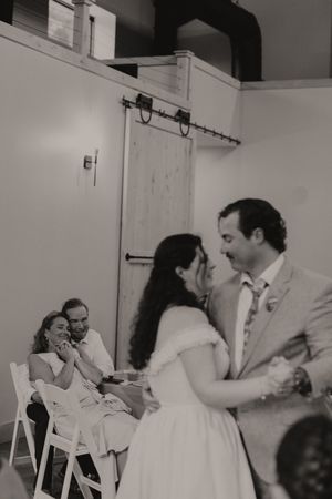 Black and white photo of a bride and groom sharing their first dance at a rustic barn wedding reception.