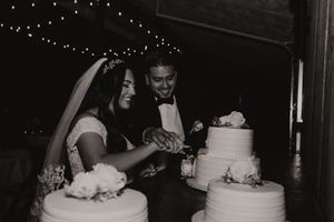 A black and white photo of a bride and groom cutting their elegant three-tiered wedding cake together at their reception.