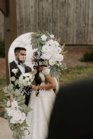 Decorative wedding welcome sign with floral accents and mirror reflection.