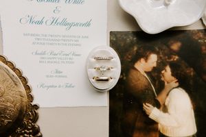 Wedding invitation for Rachel White and Noah Hollingsworth displayed with diamond rings and a vintage couple photograph.