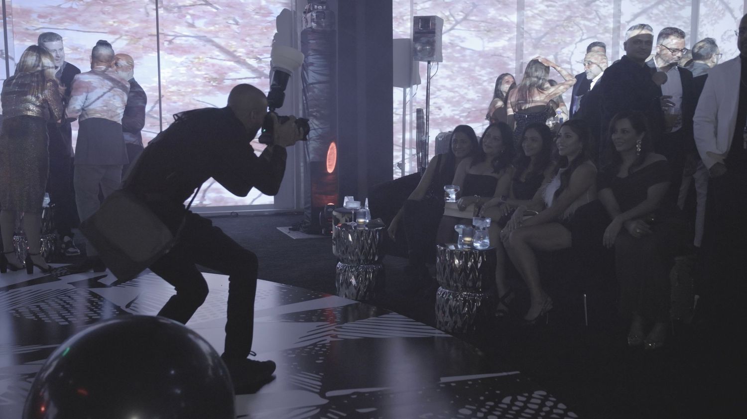 A dark silhouette of a crowd watching a presentation or event in a dimly lit auditorium space.