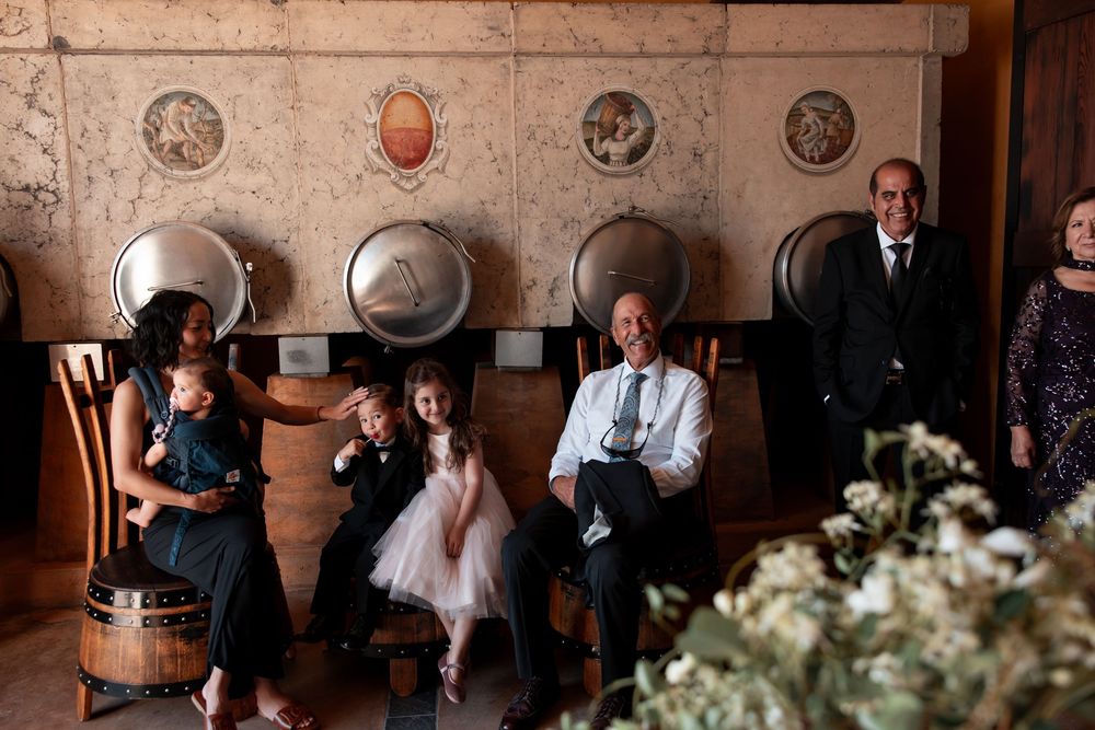 Wedding guests sit on vintage leather chairs against a wall decorated with antique plates and floral arrangements.