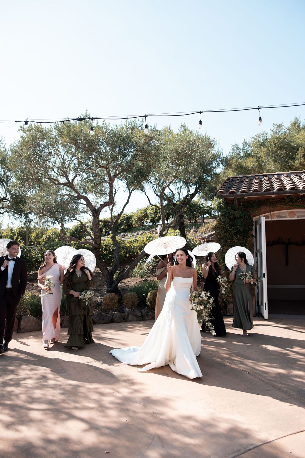 A sequence of outdoor wedding photos with people gathered under string lights and olive trees at a Spanish-style venue.