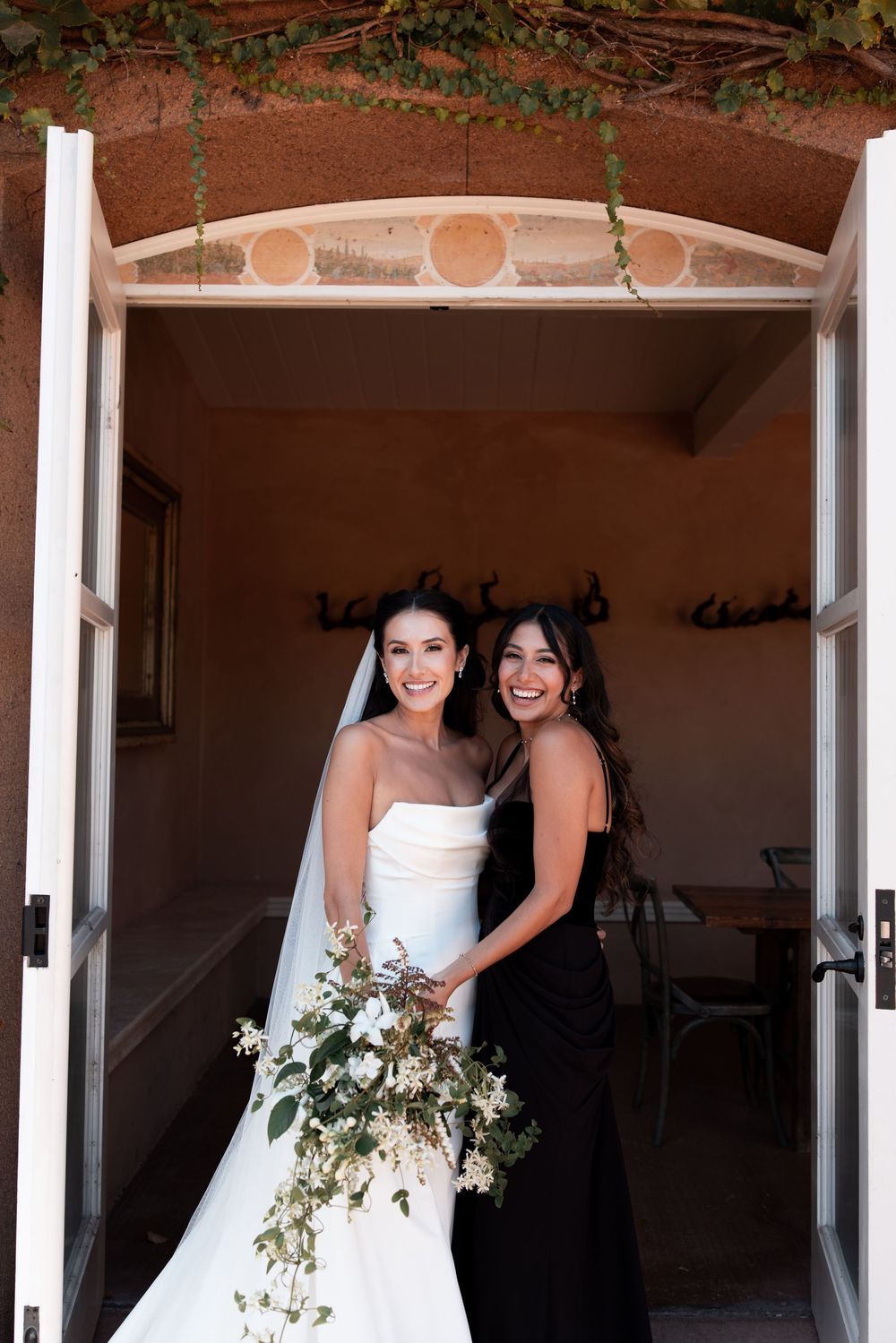 Three elegant bridal figures in white dresses stand in an arched doorway holding floral bouquets.