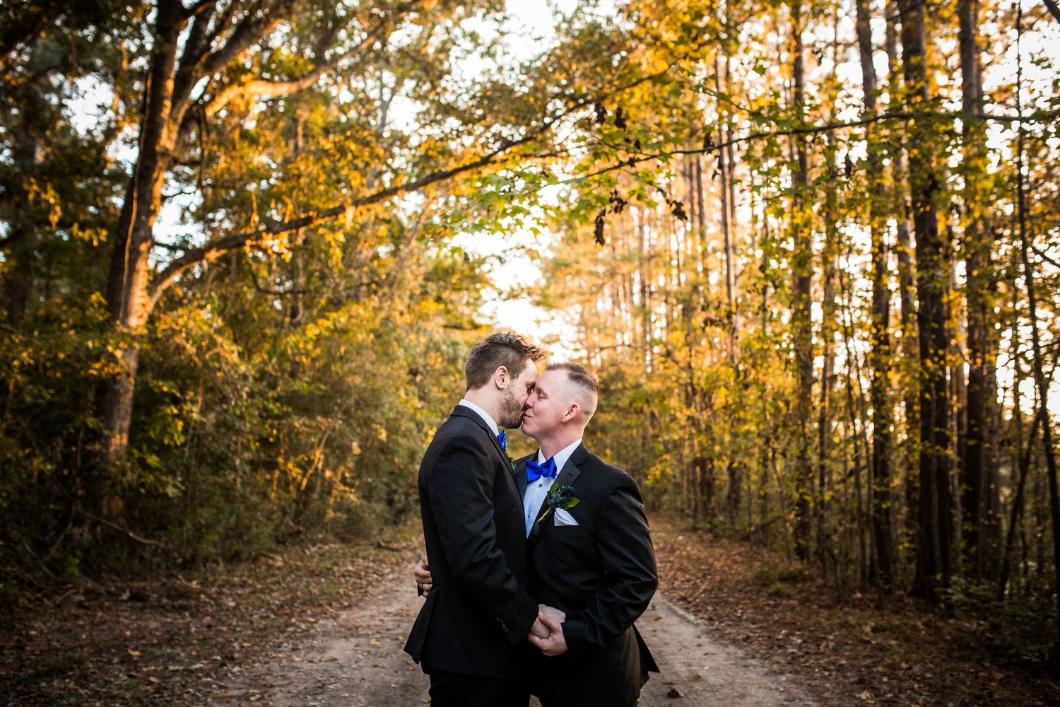 A romantic moment between a couple on a wooded path surrounded by golden autumn foliage at sunset.