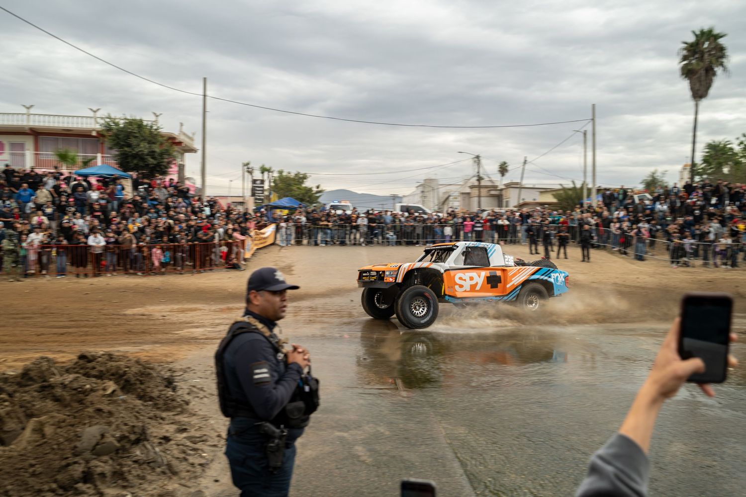 Spectators and photographers capturing off-road racing action at a dirt track event.