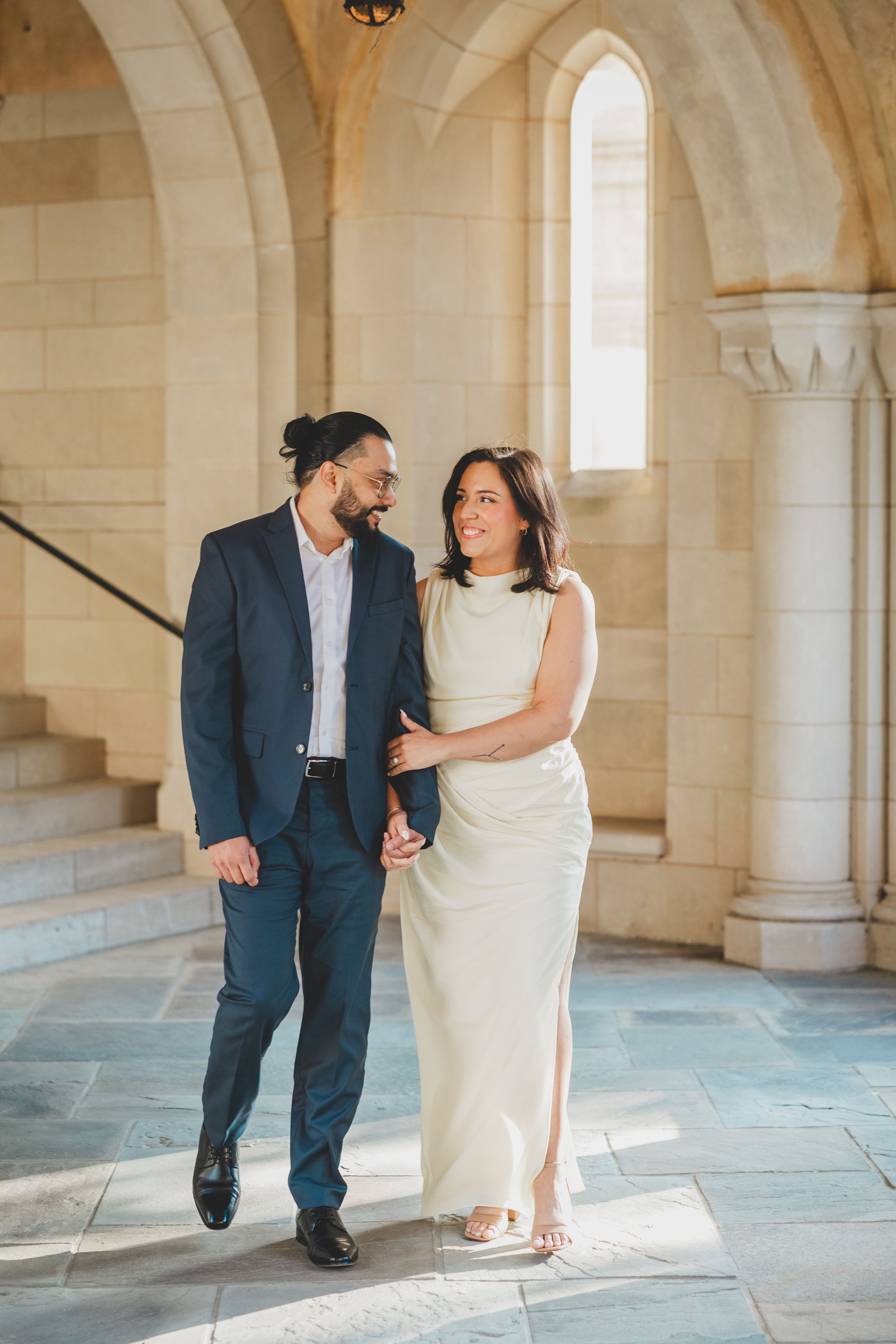 A couple shares a romantic moment in a light-filled stone hallway at the Washington National Cathedral