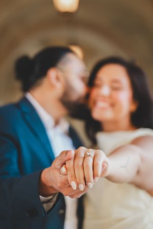 Close-up of engaged couple holding hands and showing off wedding rings while sharing an intimate moment.