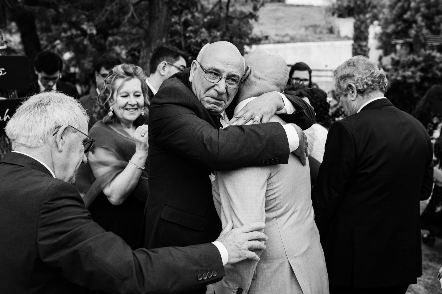 Black and white wedding photo showing people embracing and celebrating at an outdoor reception.