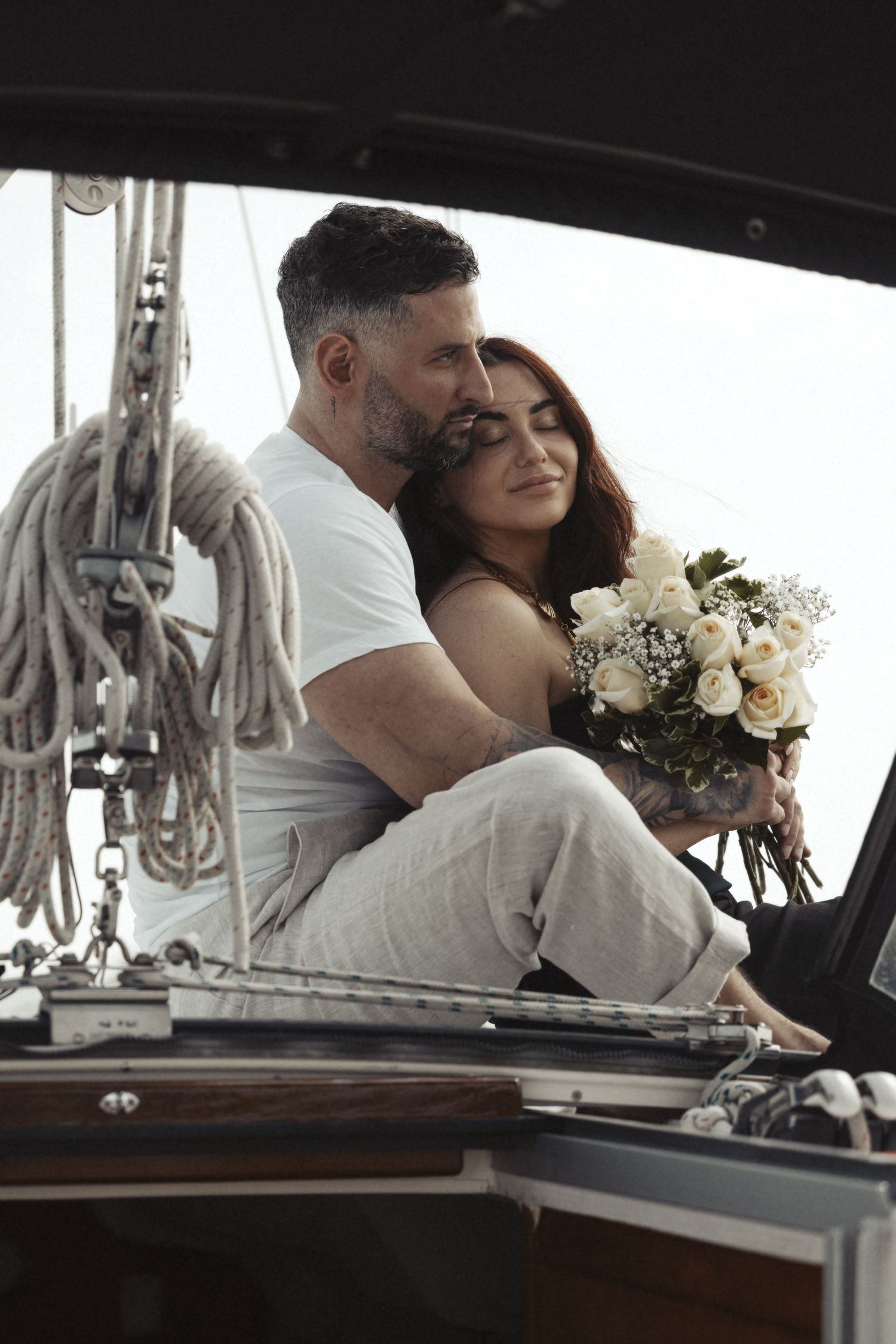 Romantic couple embracing on a boat deck with white floral bouquet and nautical elements.