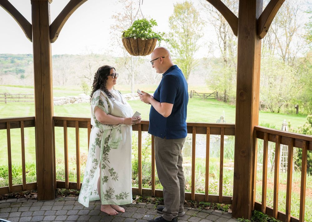 Couple exchanging vows on a wooden gazebo overlooking a scenic green countryside.
