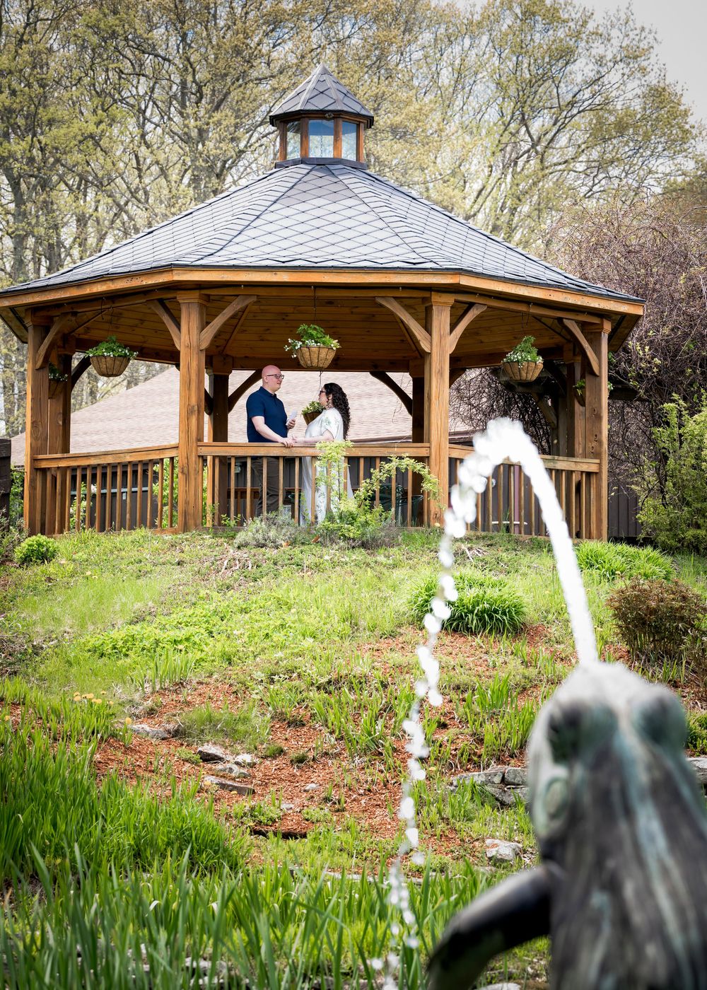 Couple sharing a romantic moment inside a wooden gazebo surrounded by lush spring gardens.
