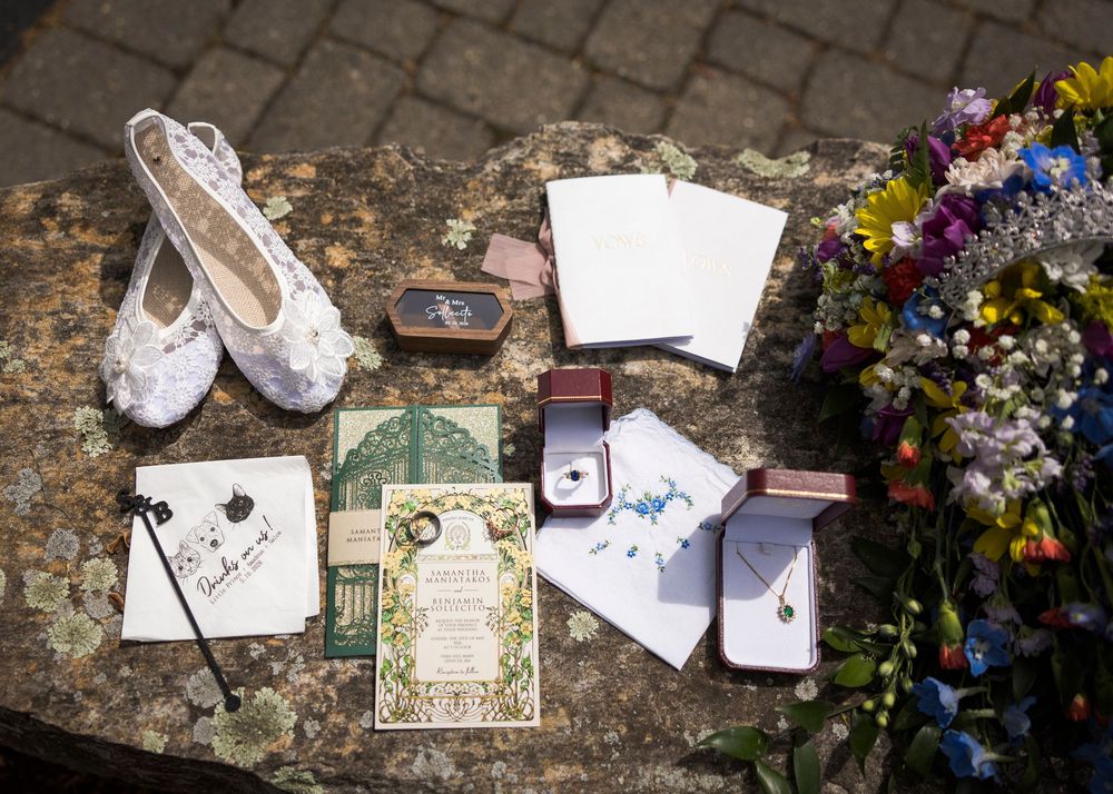 Flat lay of wedding details including lace shoes, floral invitations, rings, and colorful bridal bouquet.