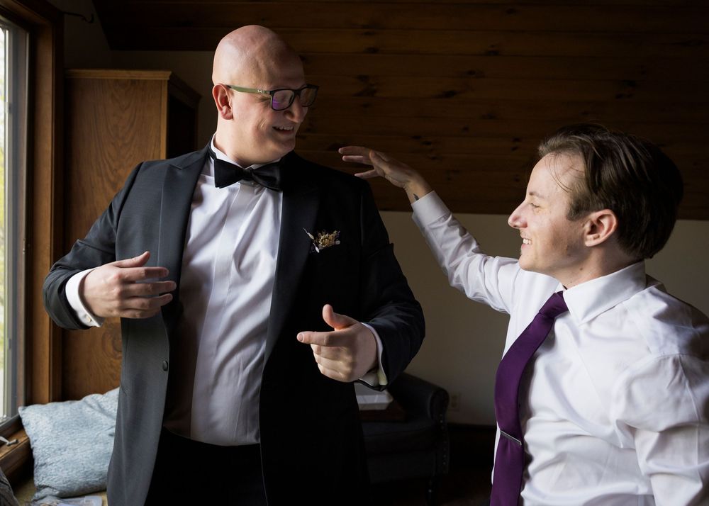 Groom in black tuxedo getting ready with groomsman adjusting his jacket before wedding.