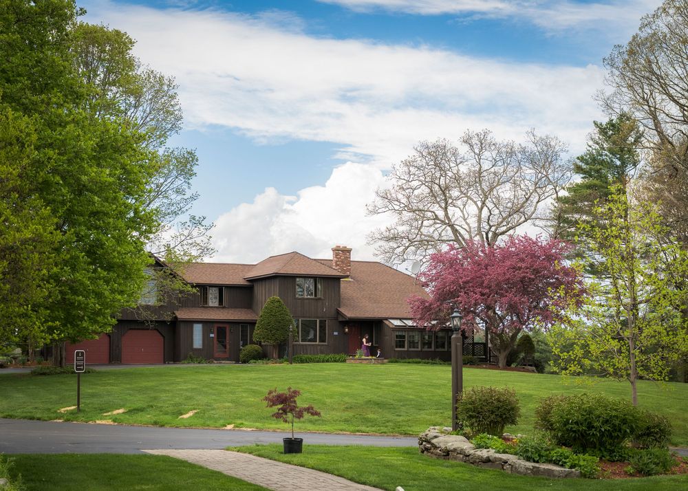 Spacious brick ranch-style home surrounded by lush green lawn and blooming spring trees under a partly cloudy sky.