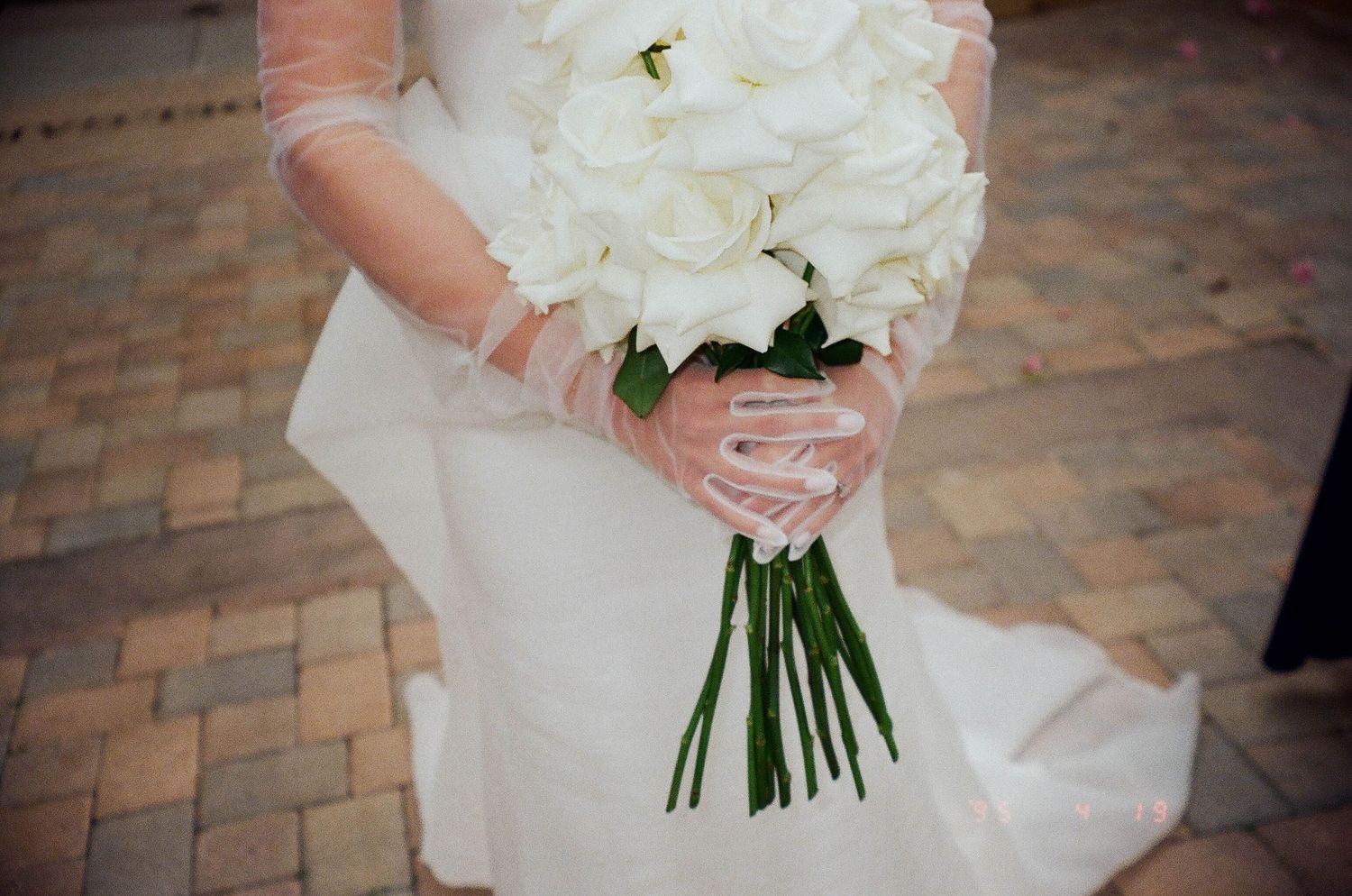 A close-up of a white bridal bouquet held against a flowing wedding dress.