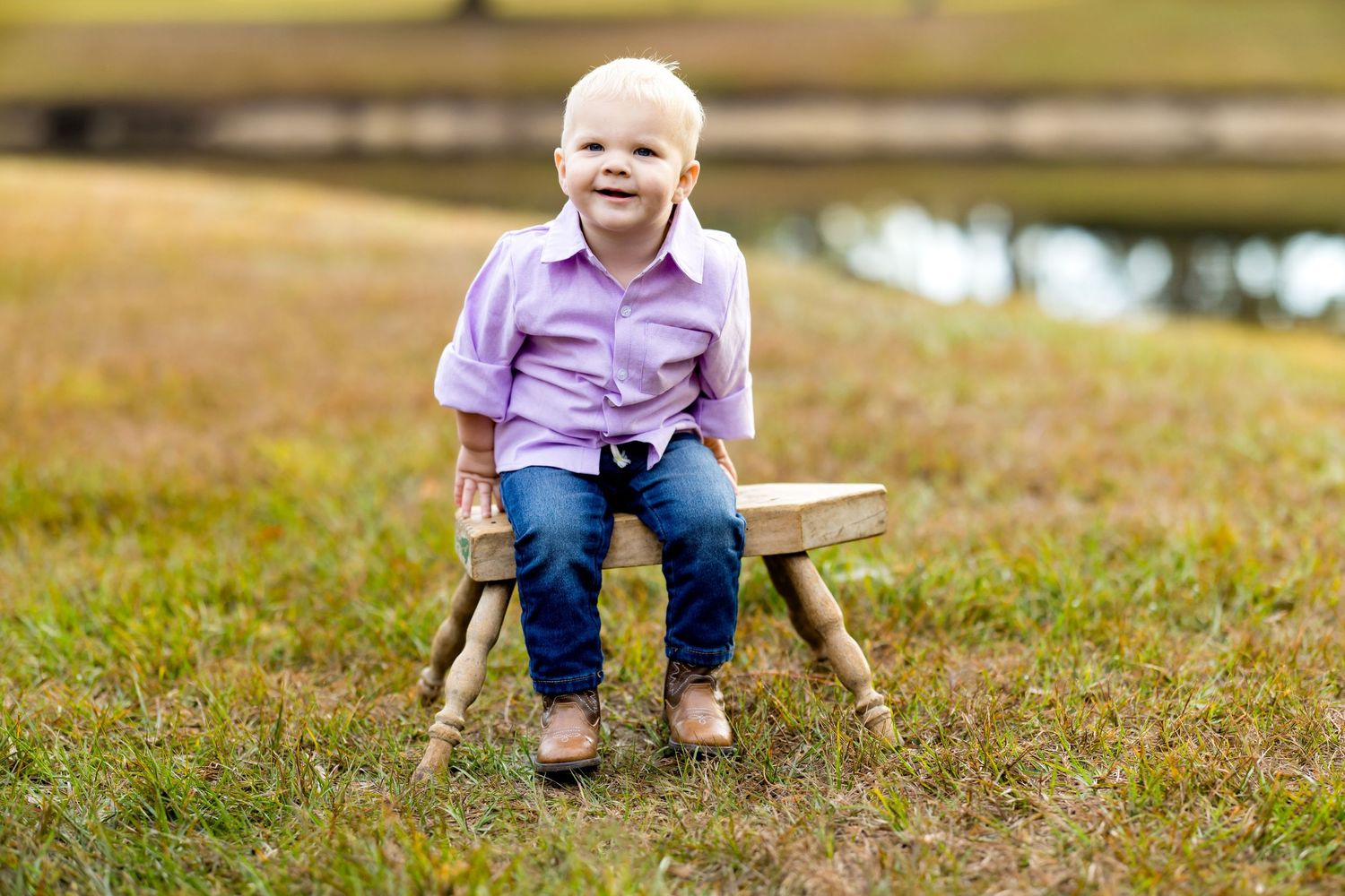A small child wearing pink and blue sits on a wooden bench in a grassy outdoor setting.