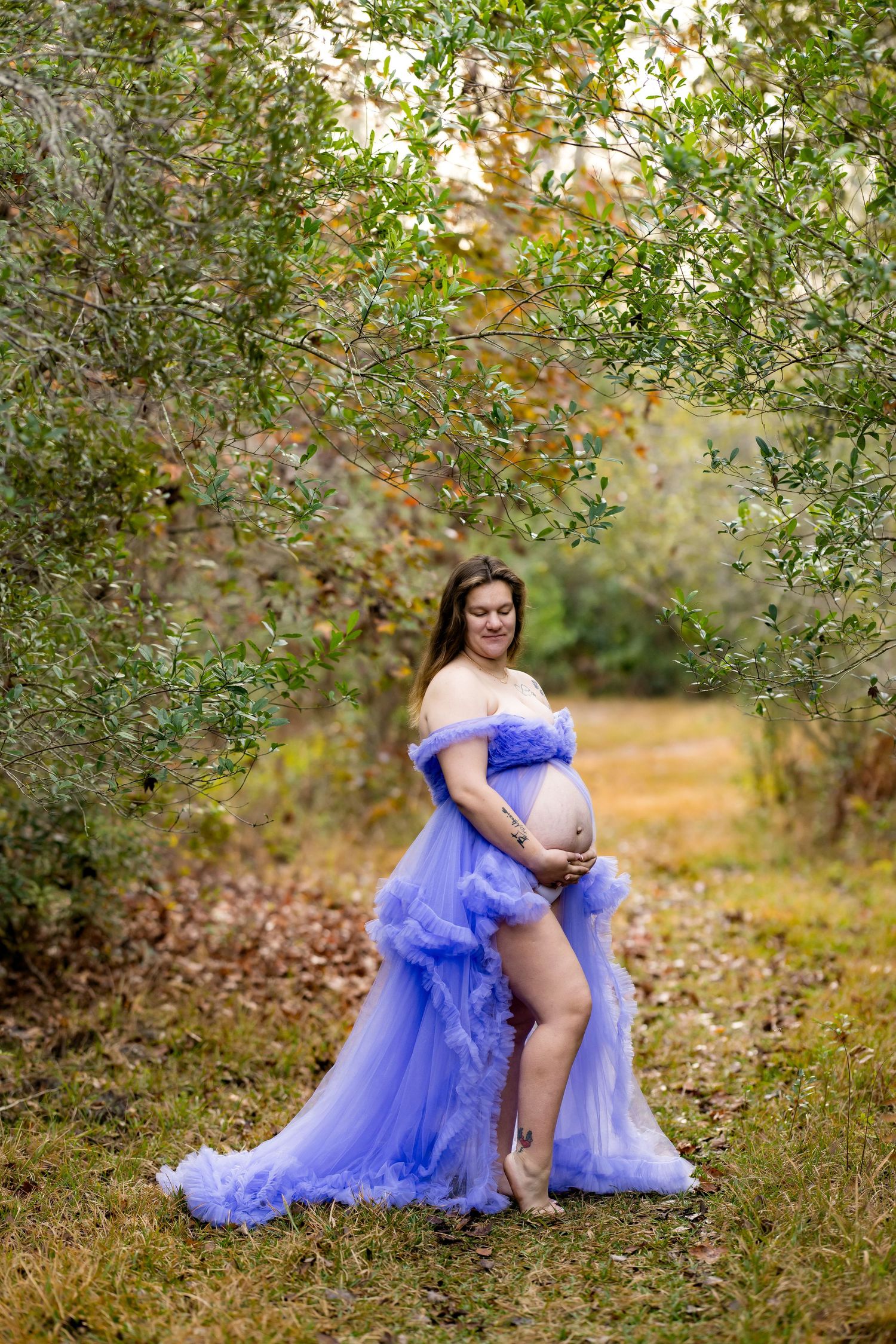 A person in a flowing royal blue tulle dress poses gracefully in an autumn garden setting.