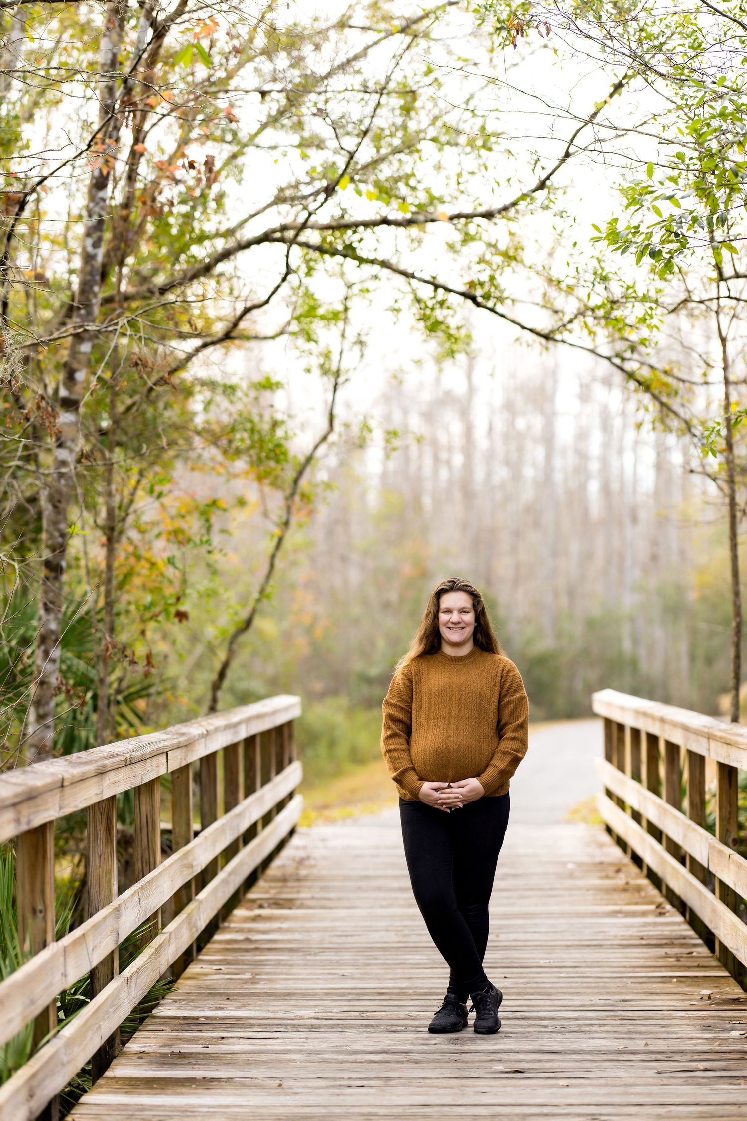 A wooden boardwalk path through autumn trees with soft misty lighting creates a peaceful natural setting.