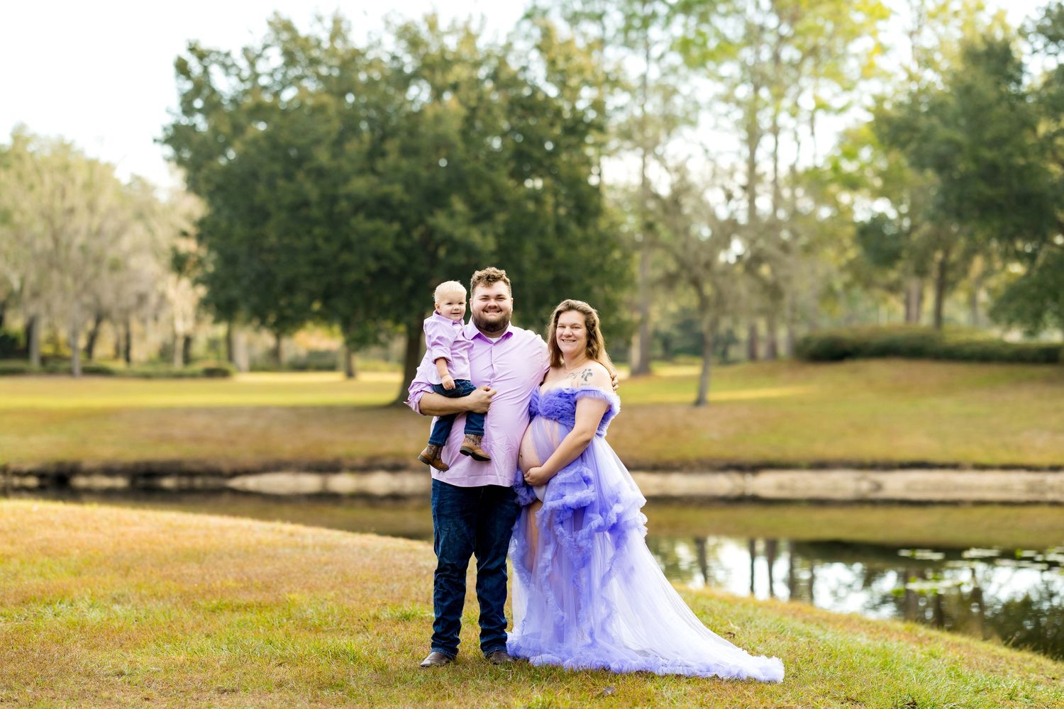 A romantic outdoor wedding photoshoot by a lake with trees and natural scenery in the background.