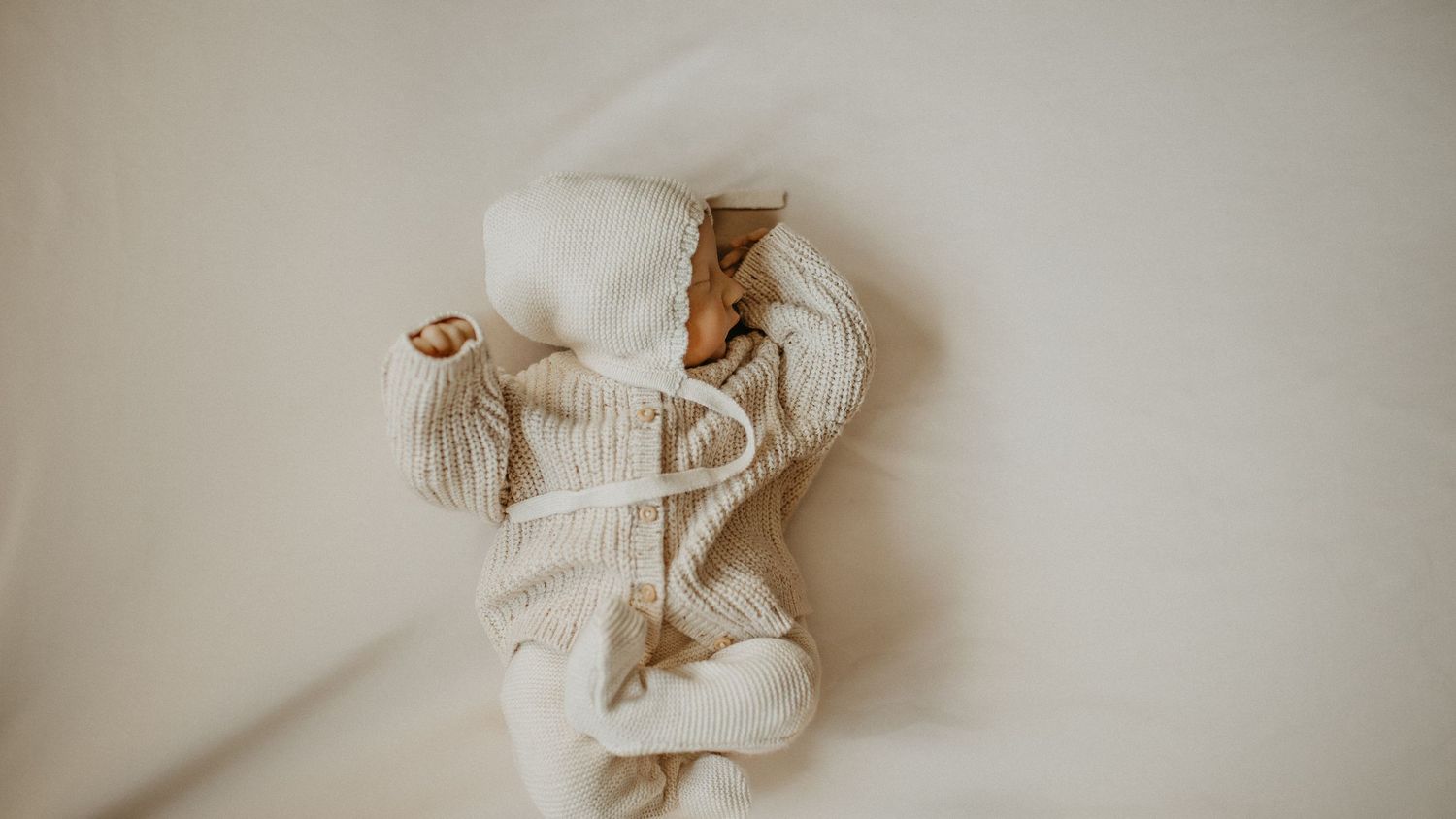 A sleeping newborn baby wrapped in soft brown swaddle cloth against a neutral background.