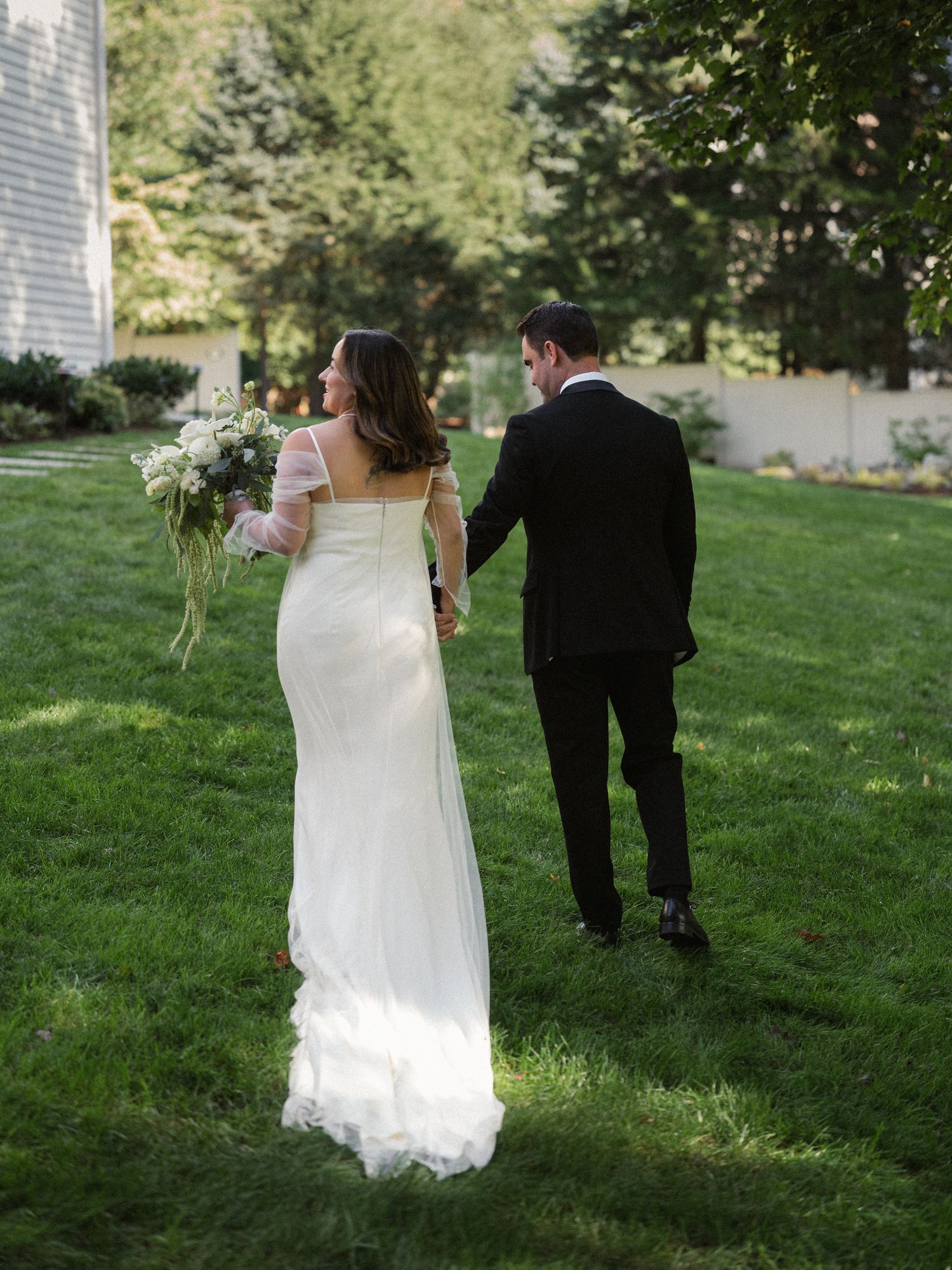 Bride and groom walk together on lush green grass during an outdoor wedding photoshoot.