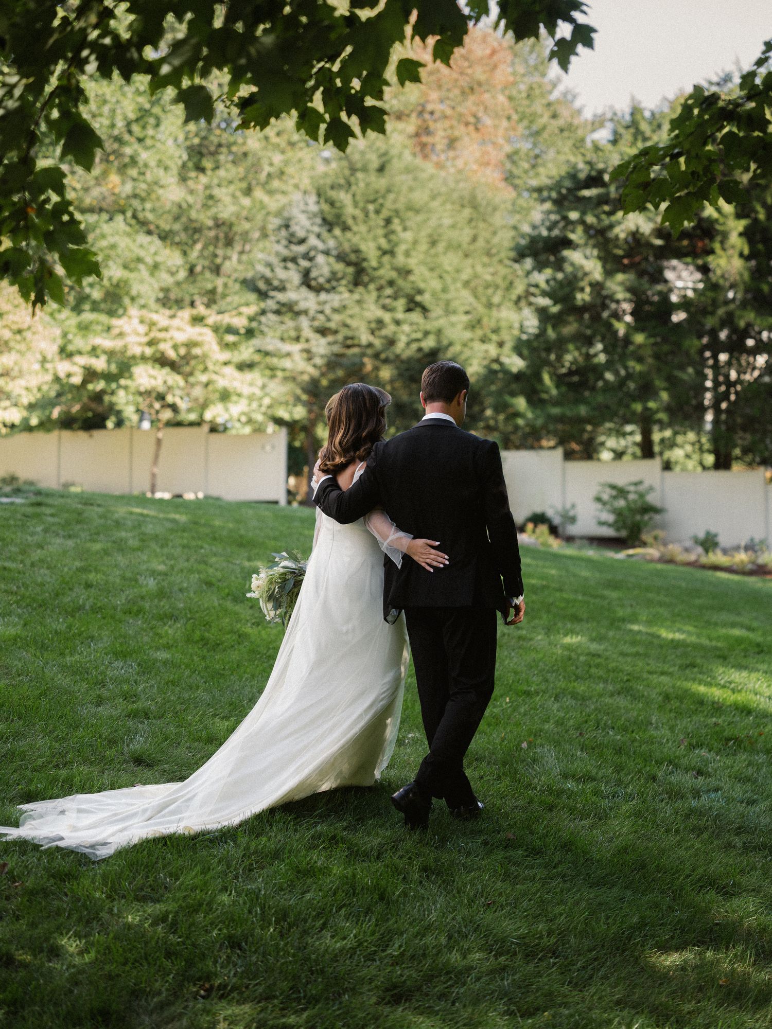Wedding couple walking together on a lush green lawn with trees in the background.