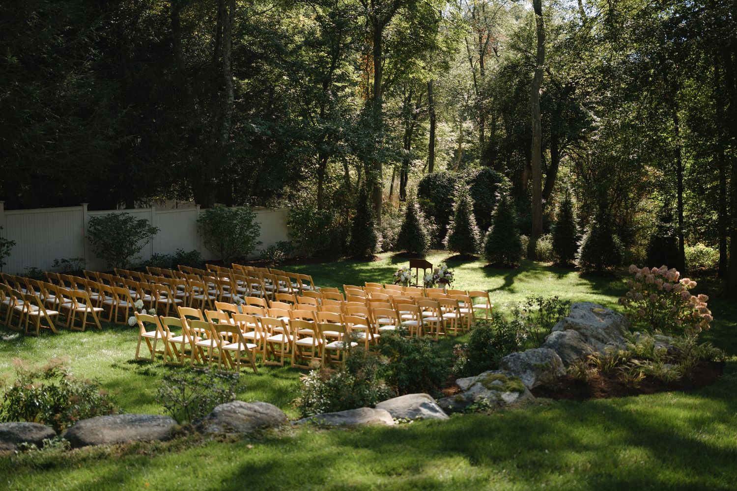 Panoramic view of wooden chairs set up for an outdoor garden wedding ceremony.