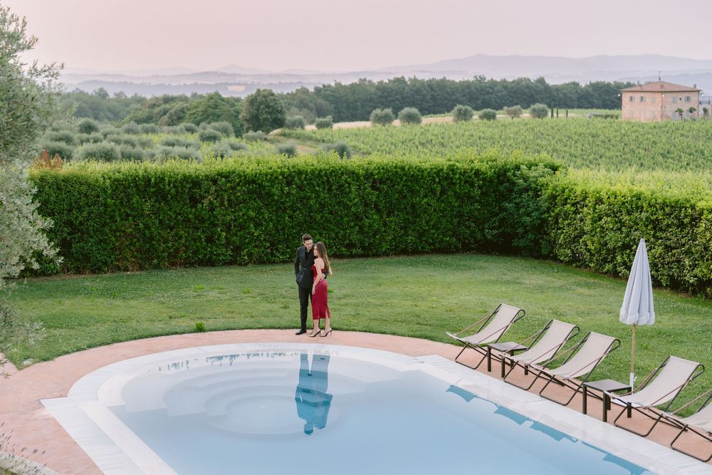 Tranquil infinity pool overlooking scenic Tuscan countryside with lounge chairs and cypress trees at sunset.