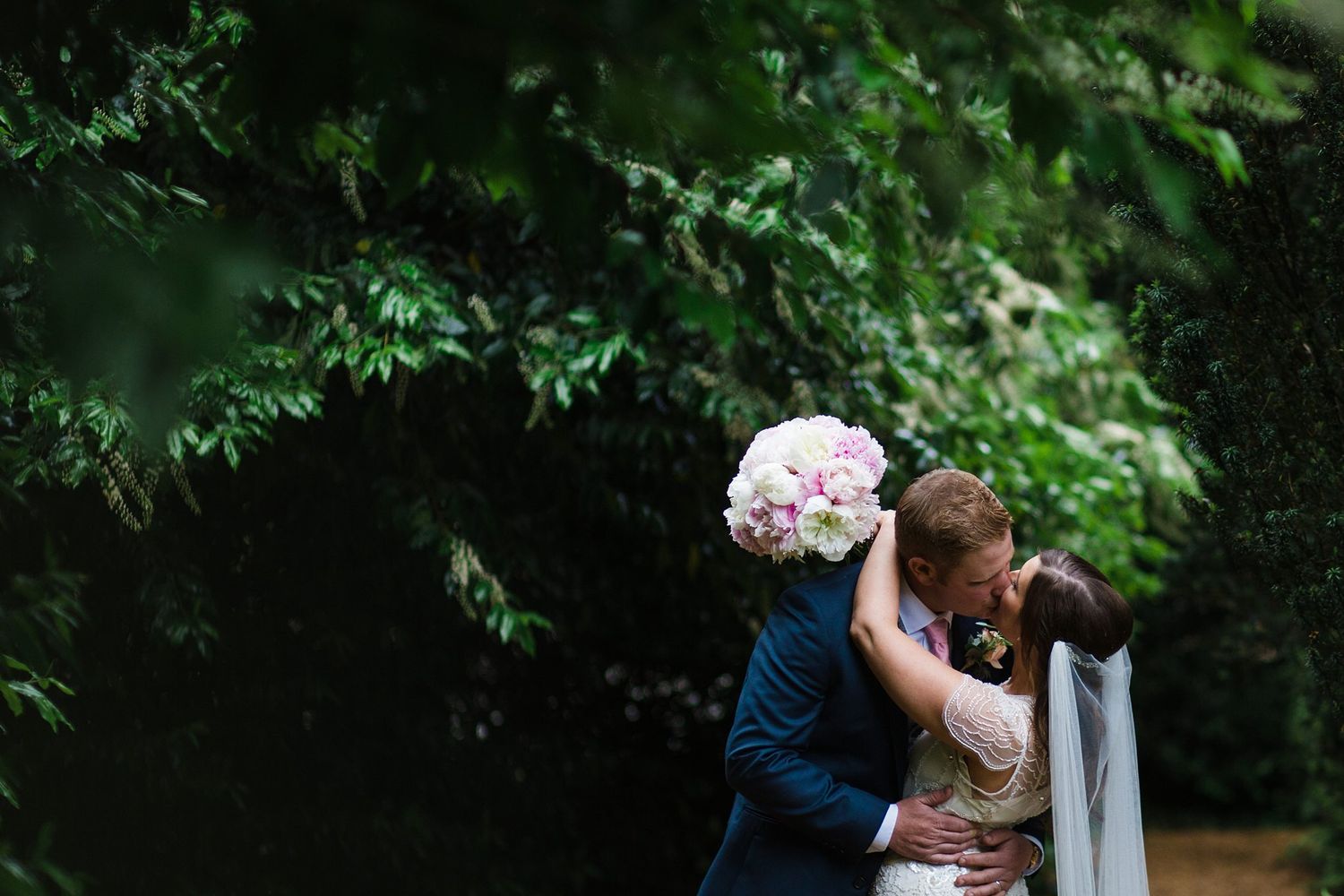 Bride and groom sharing a romantic kiss surrounded by greenery on their wedding day