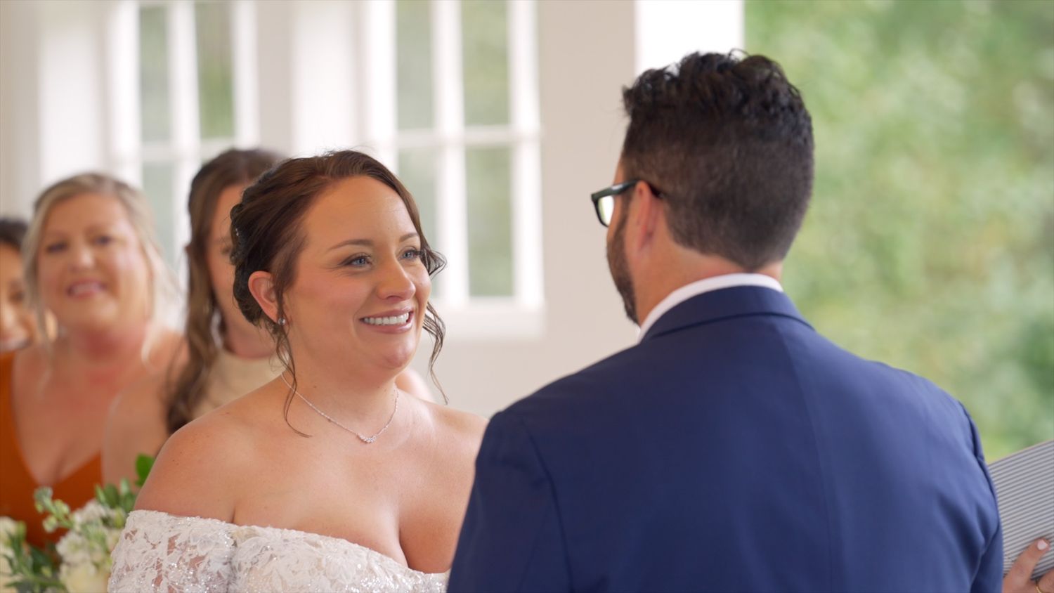 Wedding guests mingle and converse during an elegant indoor reception with natural lighting through windows.
