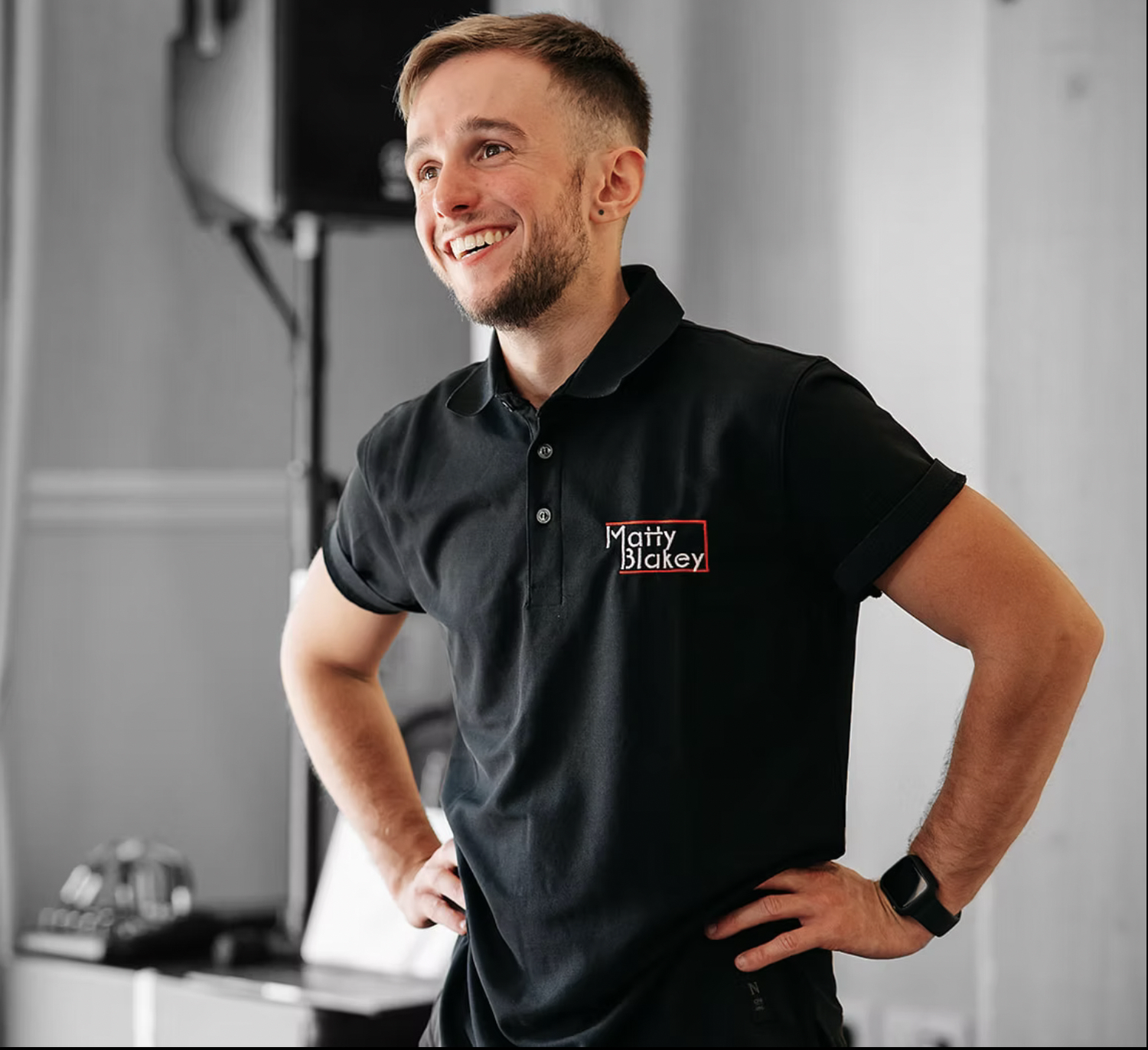 A chef in a black uniform smiles while standing in a professional kitchen setting.