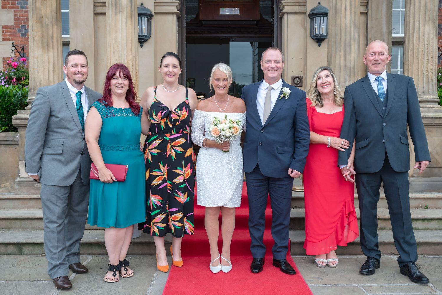 Wedding party members pose in formal attire outside a grand stone building with elegant architecture and lanterns.