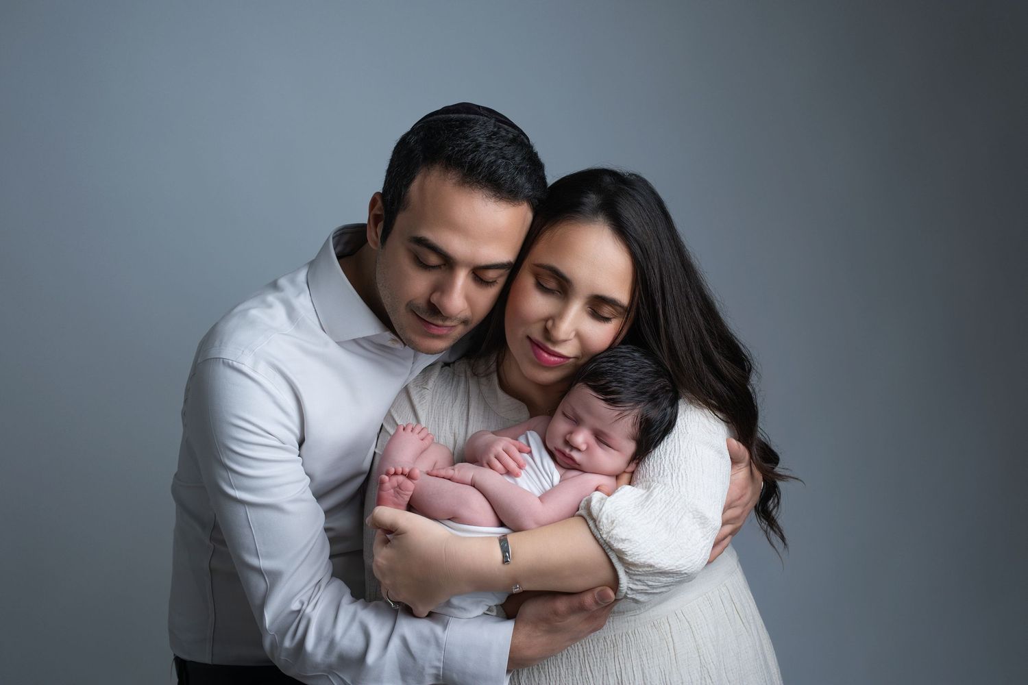 Posed studio portrait of parents cuddling their newborn baby during family photography session