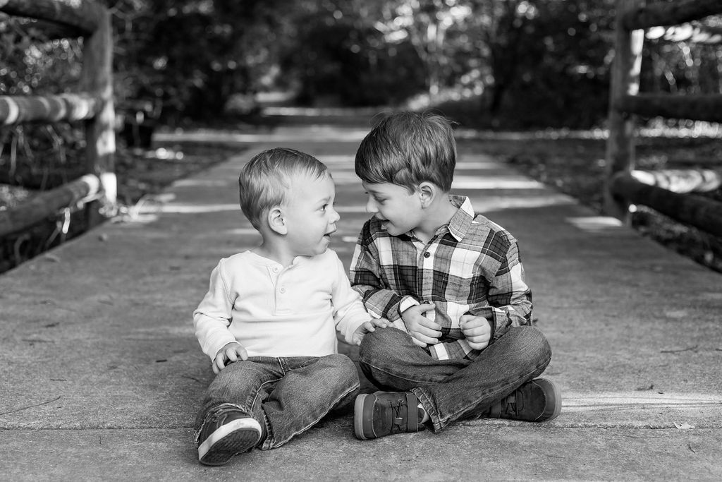 Two young children sit together on a pathway sharing a tender moment in black and white photography.