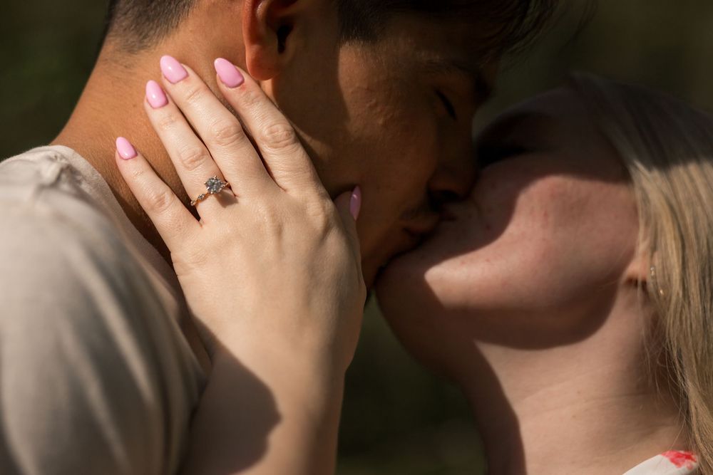 Close-up of a couple sharing a kiss, with the woman showcasing a beautiful diamond engagement ring on her hand.