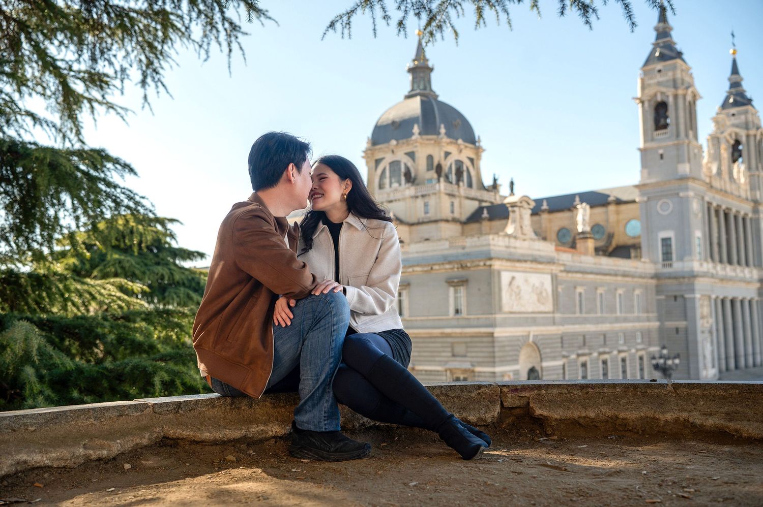A couple shares a romantic moment at sunset overlooking the historic Royal Palace of Madrid and Almudena Cathedral.