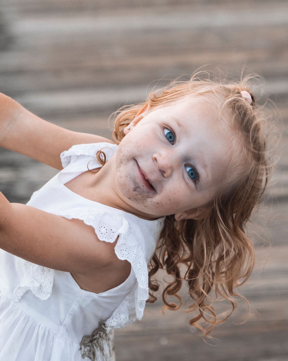 Adorable toddler girl with curly hair in white dress smiling outdoors.