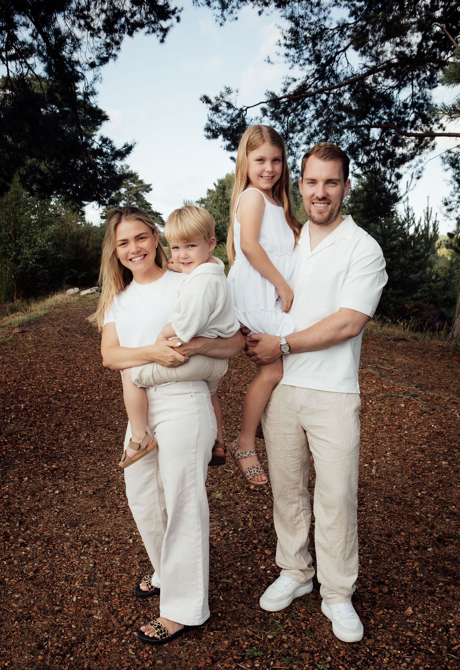 Photo of a family of four in a woodland setting.  The mum and dad are holding their children and they are all smiling.