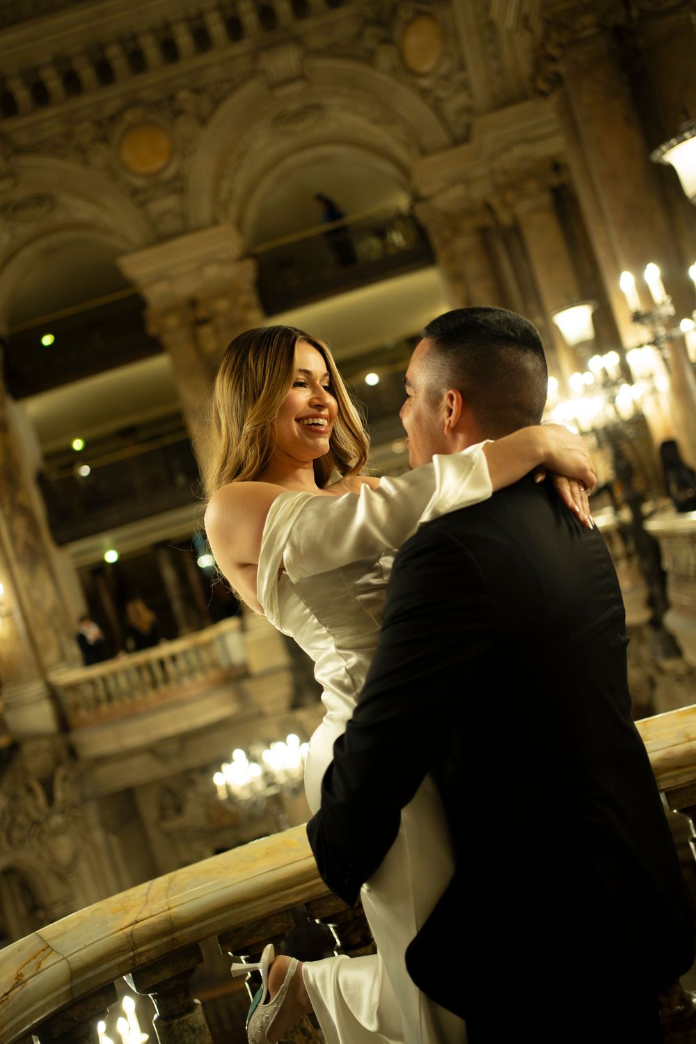 A couple shares a romantic dance moment in an elegant ballroom with ornate architectural details and warm lighting.