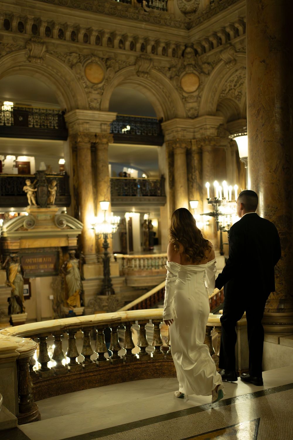 People admiring ornate architecture and decorative details inside the grand Opera Garnier in Paris at night.