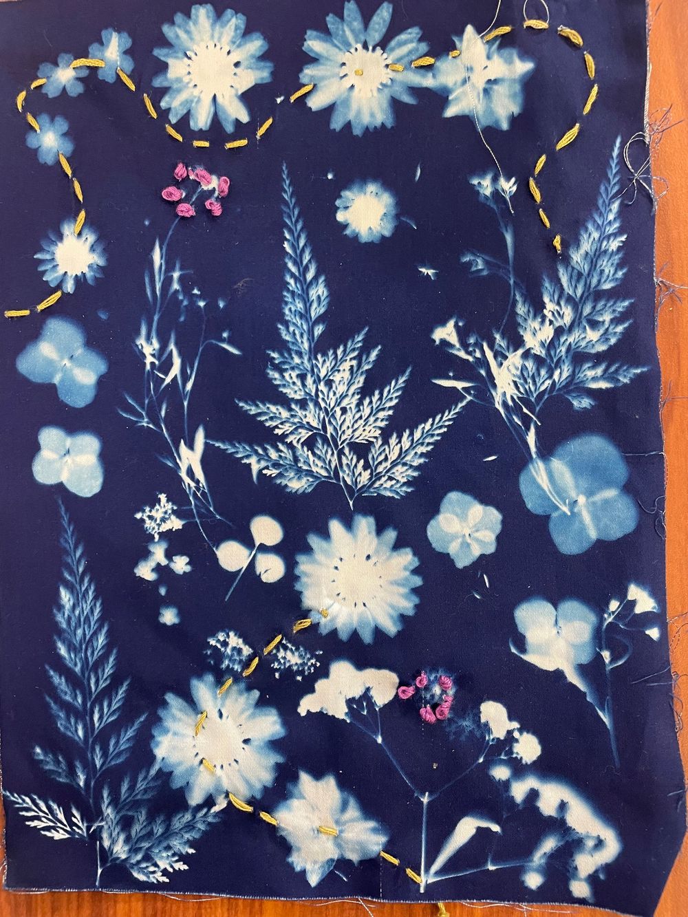 Cyanotype print featuring delicate white and blue floral arrangements with ferns against a deep navy background.