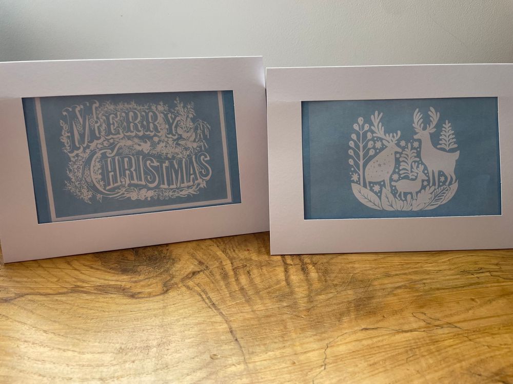 A series of decorative Christmas-themed paper cut signs displayed against a light wooden background.